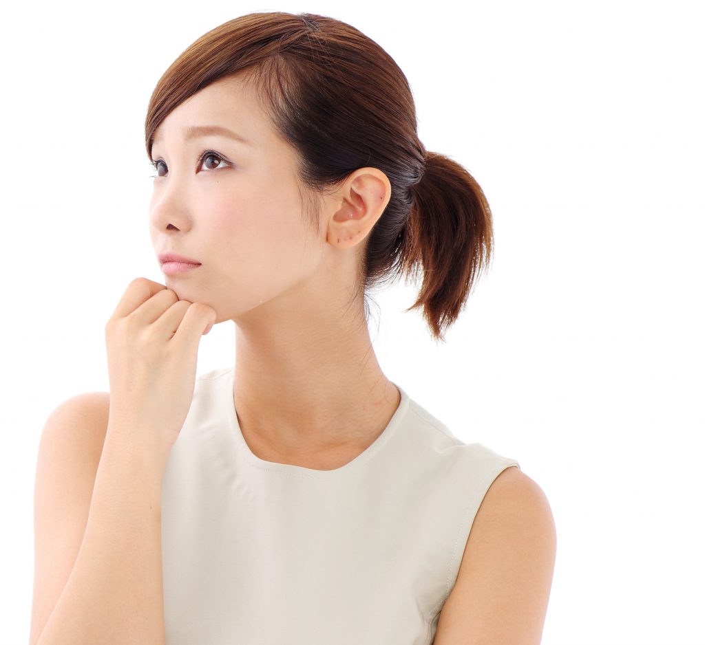 Young Asian woman in white dress holding hand to chin in pensive expression