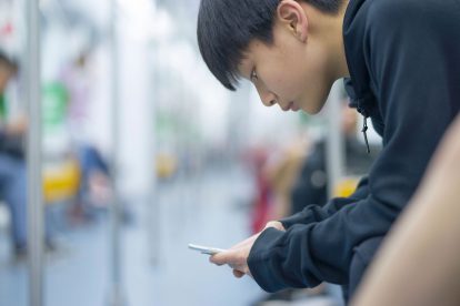 Teenage boy sitting on public transport using smartphone to access social media