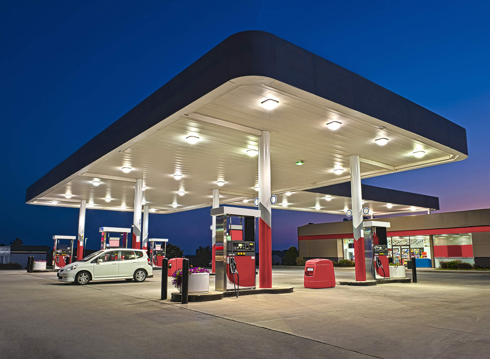 Petrol station at dusk with cars visible on forecourt and shop at the rear