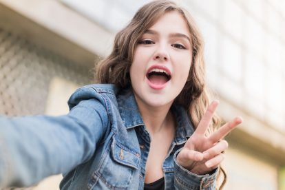 Teenager making peace sign with one hand while holding other hand out to make selfie video