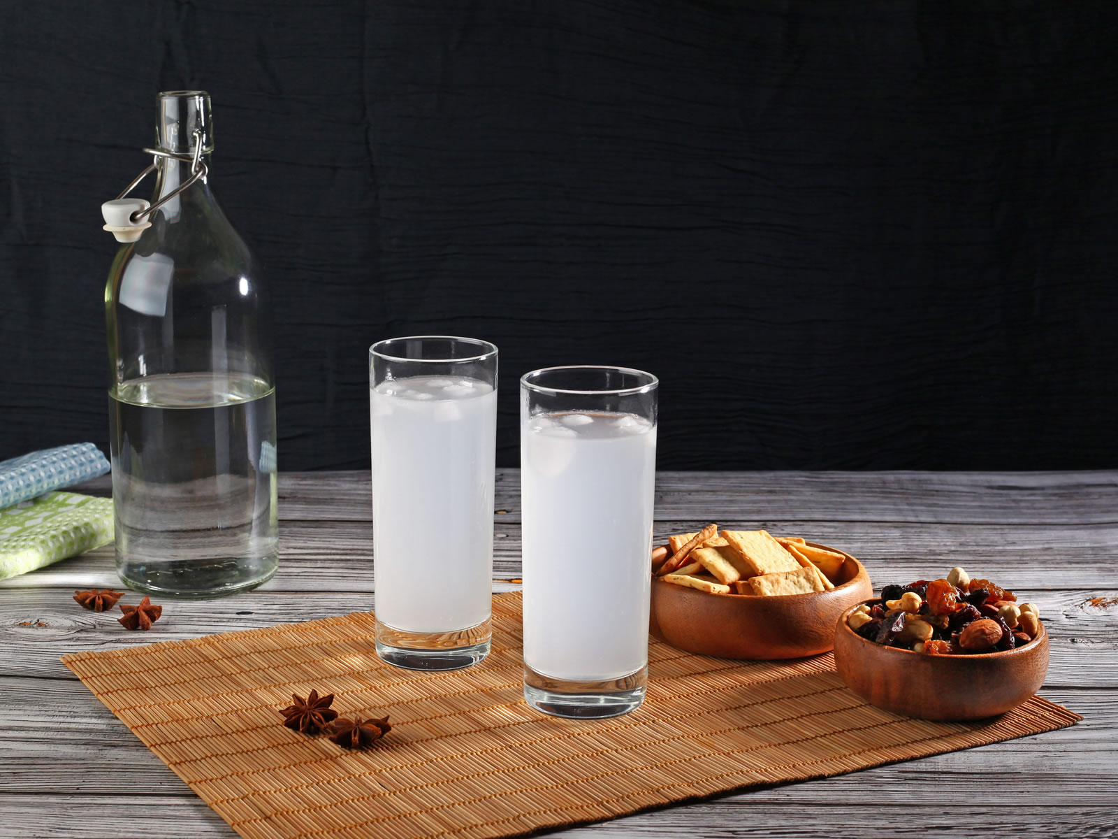 Two glasses of Turkish raki on a table with bowls of snacks and an open bottle of water in the background