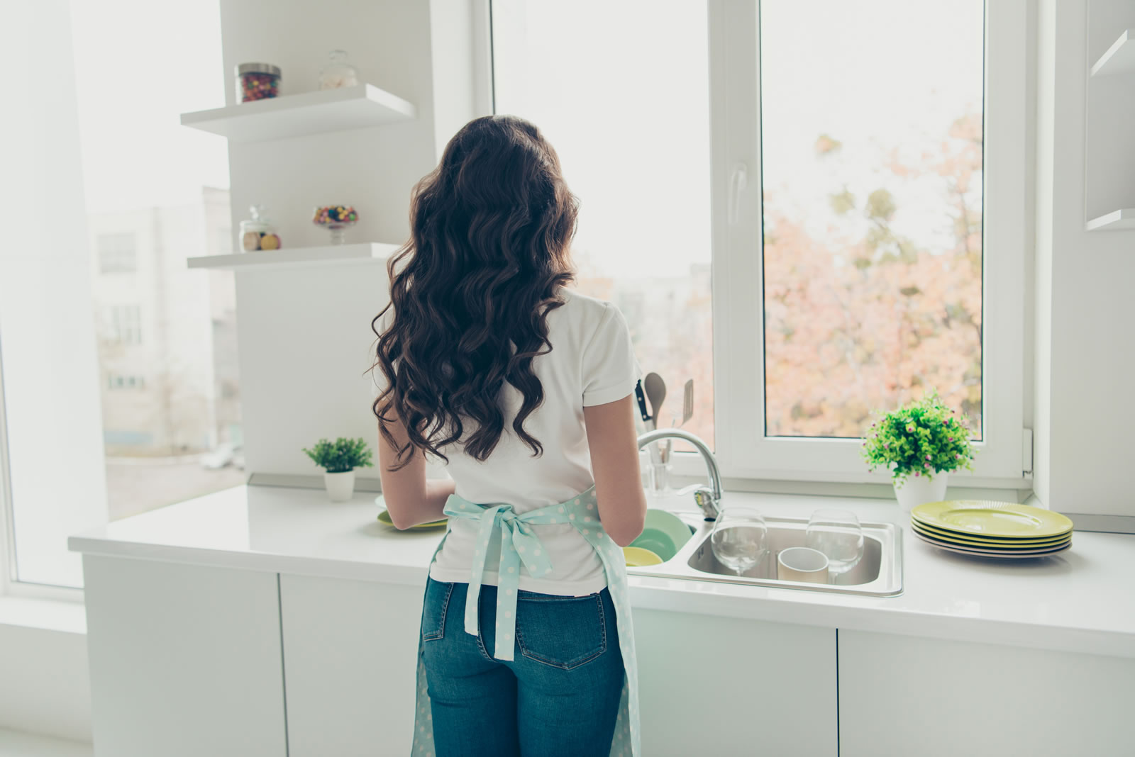 Woman testing medical packaging at kitchen sink, viewed from behind
