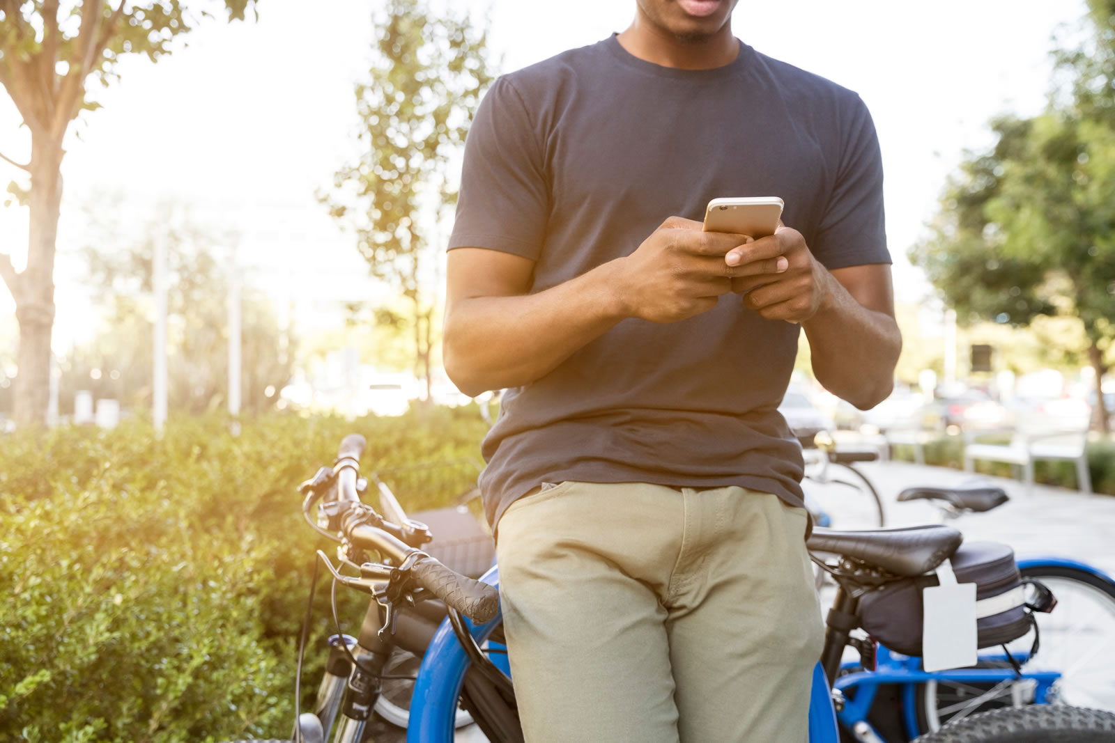 Young male online bulletin board respondent submitting entry on his smartphone while standing in front of his bicycle